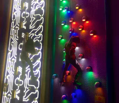Child climbing up a vibrant neon-lit interactive indoor climbing wall attraction.