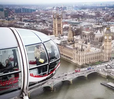 View from a high angle looking down at a glass passenger capsule on the London Eye overlooking the River Thames and city skyline.