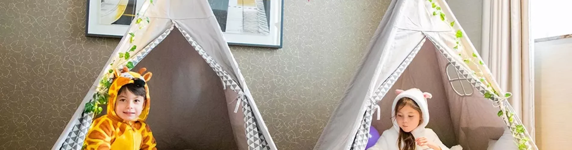 An ultra-luxury children's in-suite movie night teepee glamping setup at the Conrad London St. James hotel featuring two kids in animal onesies with popcorn.