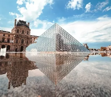 The iconic glass pyramid of the Louvre Museum reflecting perfectly in the surrounding water fountains on a clear day in Paris.