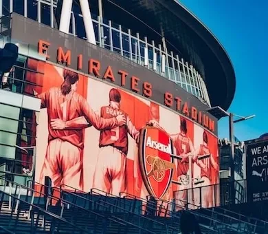 The exterior of the Emirates Stadium with a large red banner displaying Arsenal football players.