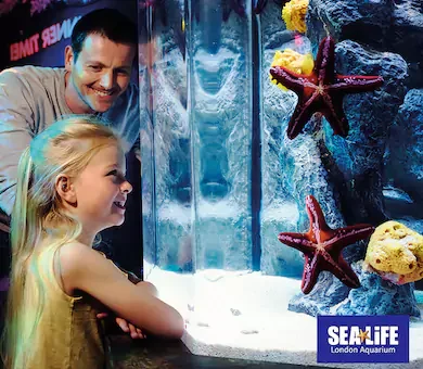 Young girl with her father discovering marine life and starfish exhibits at the SEA LIFE London Aquarium.