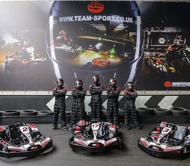 Children in racing suits standing behind a row of racing karts at Team Sport indoor go karting arena.