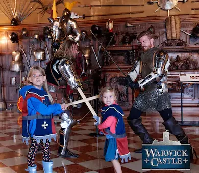 Young children interacting with historical knights in armor during a family day out at Warwick Castle.